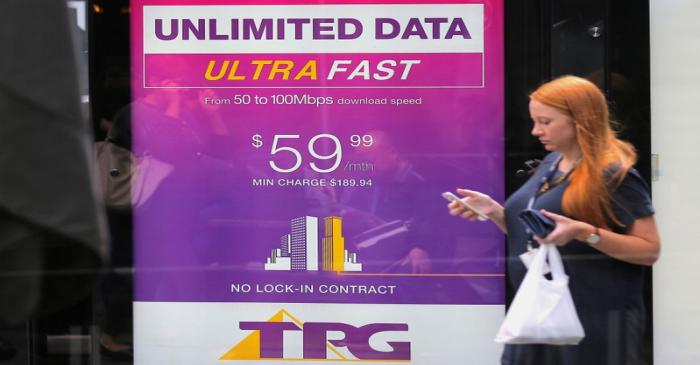 FILE PHOTO: A woman looks at her phone as she walks past an advertisement for Australia's TPG