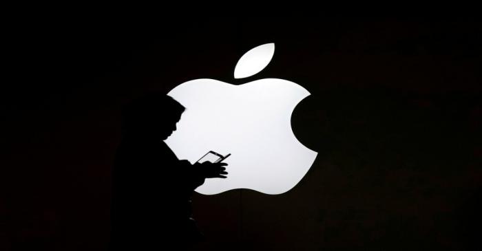 FILE PHOTO: A woman looks at the screen of her mobile phone in front of an Apple logo outside