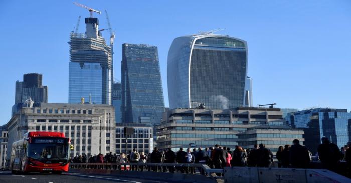 Workers are seen crossing London Bridge with City of London skyscrapers seen behind during the