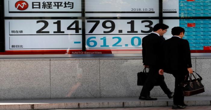 Men walk past an electronic board showing Japan's Nikkei average outside a brokerage in Tokyo