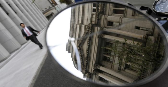 The Bank of Japan building is reflected in a mirror as a man walks past in Tokyo