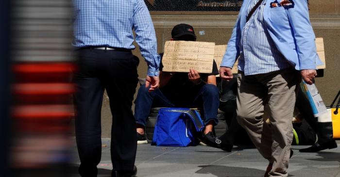 Pedestrians walk past a man holding a sign as he begs for money on a main street in the central