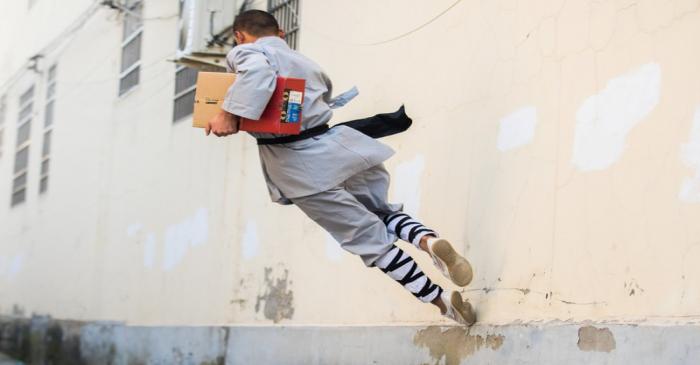 Man dressed in a kung fu costume displays his martial art skills as he delivers a parcel ahead
