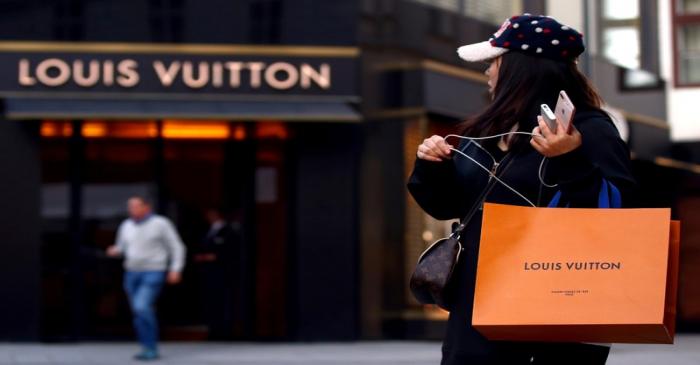Woman with a Louis Vuitton-branded shopping bag looks towards the entrance of a branch store by
