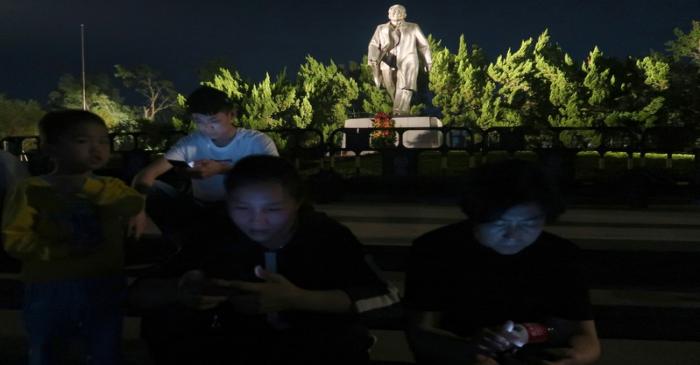 People sit on steps in front of the statue of the former Chinese leader Deng Xiaoping ahead of