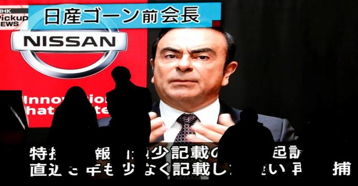 Passersby are silhouetted as a huge street monitor broadcasts news reporting ousted Nissan