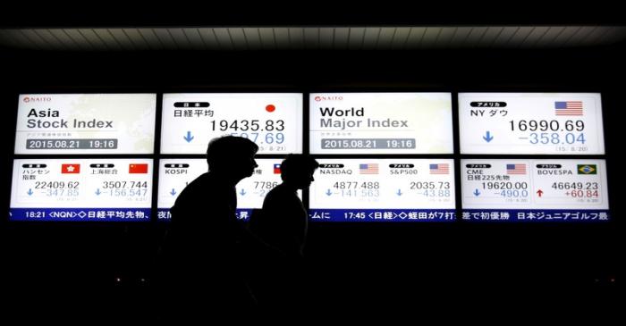 People walk past an electronic board displaying various Asian countries' stock price index and