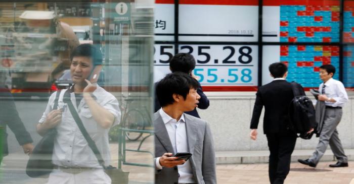 People walk past an electronic board showing Japan's Nikkei average outside a brokerage in