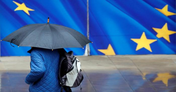 A man with an umbrella walks past the EU Commission headquarters in Brussels