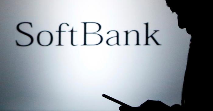 FILE PHOTO - A pedestrian holding a mobile phone walks past a logo of SoftBank Corp in front of