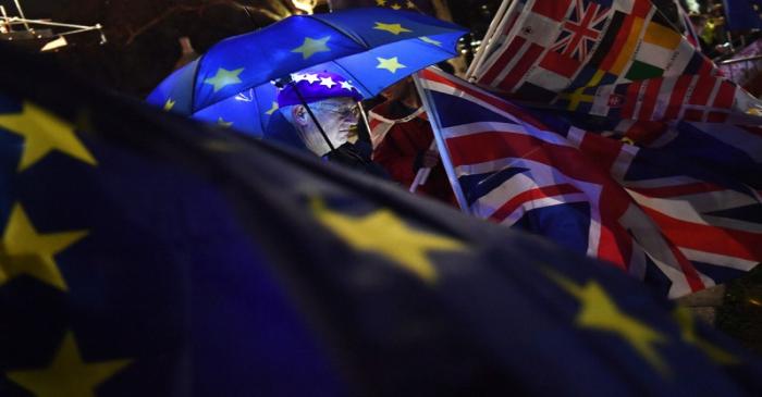An anti-Brexit protester stands with an illuminated EU umbrella surrounded in flags outside the