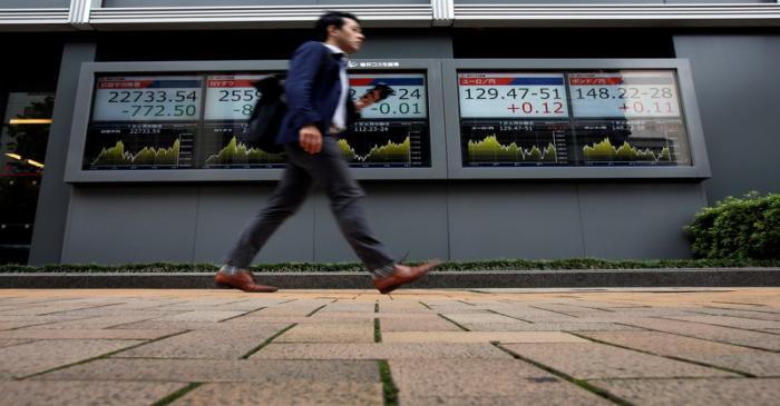 A passerby walks past an electronic boards Japan's Nikkei average, the Dow Jones Industrial