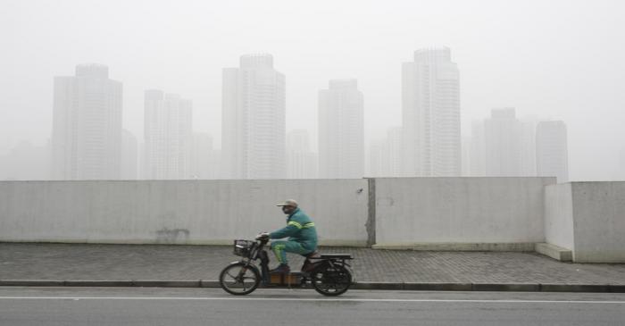 A man wearing a face mask rides an electric bicycle near the financial district of Pudong amid