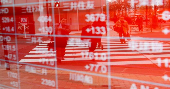 Pedestrians are reflected on an electronic board showing stock prices outside a brokerage in