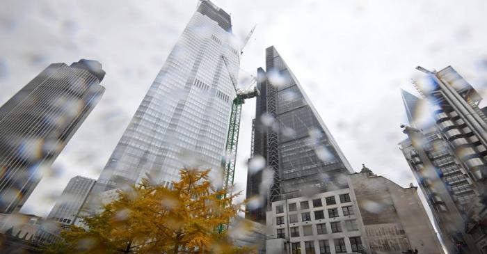 A tree covered in autumn foliage is seen with office skyscrapers around it during rainfall in