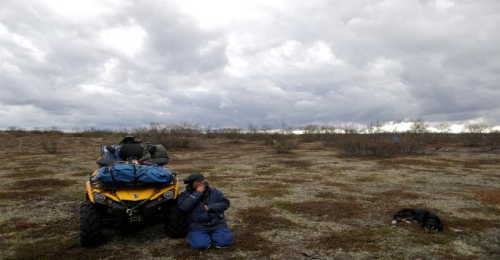 FILE PHOTO: Sami reindeer herder Nils shelters from the wind in order to smoke next to his ATV