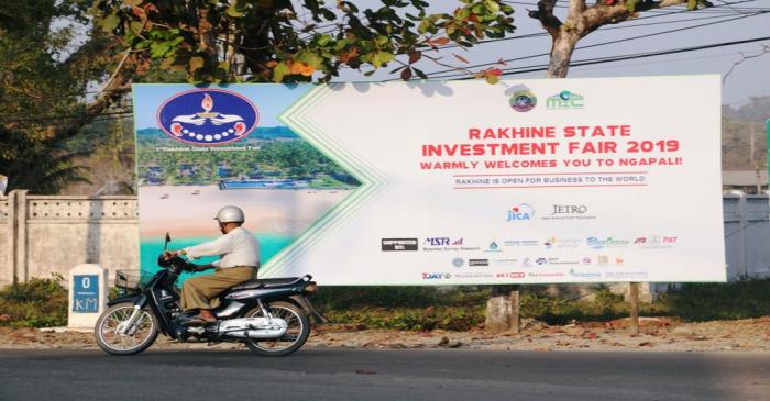 A rider passes by the Rakhine State Investment Fair 2019 bulletin board in Ngapali beach in