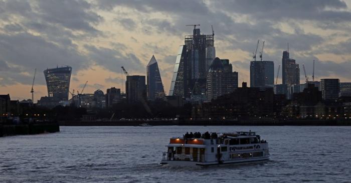 FILE PHOTO: A river boat cruises down the River Thames as the sun sets behind the Canary Wharf