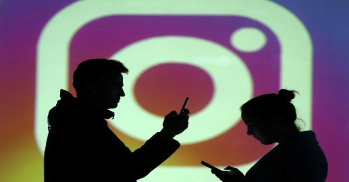 Silhouettes of mobile users are seen next to a screen projection of Instagram logo in this