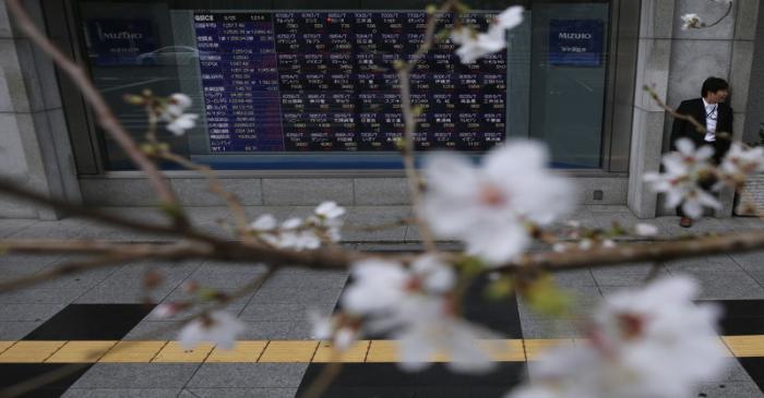 FILE PHOTO - A man stands next to an electronic stock quotation board as cherry blossoms are in
