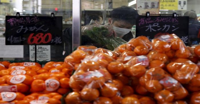 A man wearing a mask puts packs of vegetables into a plastic bag inside a supermarket at a