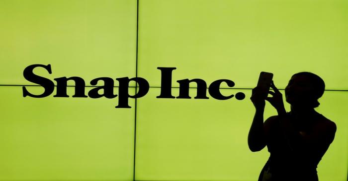 FILE PHOTO: A woman stands in front of the logo of Snap Inc. on the floor of the New York Stock