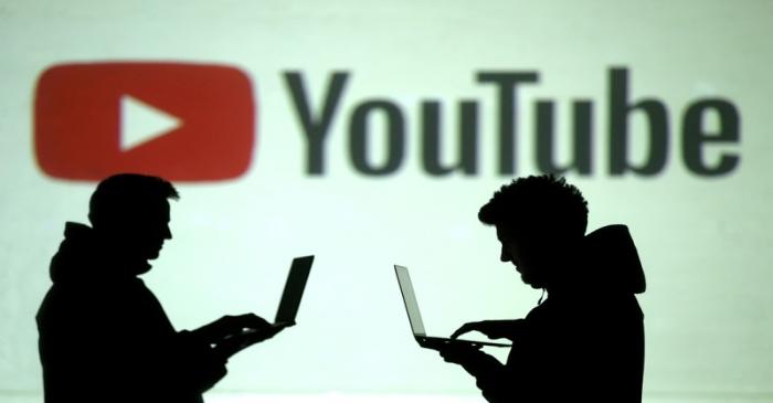 FILE PHOTO: Silhouettes of mobile device users are seen next to a screen projection of Youtube