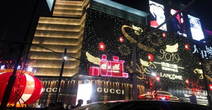 Neon signs in the shapes of luxury brand names illuminate the facade of David Plaza, a shopping