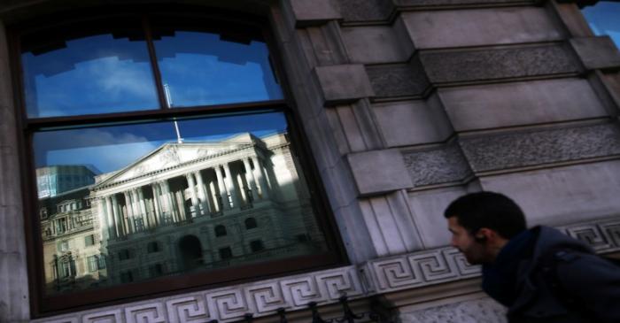 A man walks past a reflection of the Bank of England in a window in the City of London
