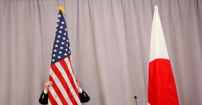 A worker adjusts the U.S. flag before Japanese Prime Minister Shinzo Abe addresses media