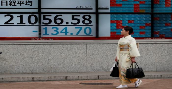 A woman wearing a kimono walks past an electronic board showing the Nikkei stock index outside