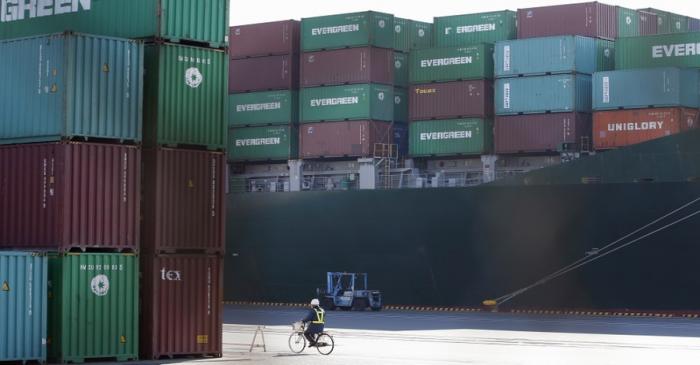 A man rides a bicycle past containers and a cargo ship at a port in Tokyo