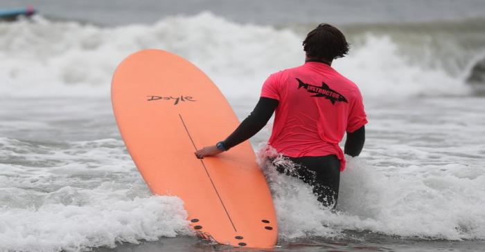 A surf instructor carries a Doyle surfboard in Malibu