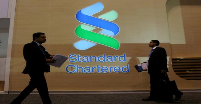 FILE PHOTO: People pass by the logo of Standard Chartered plc at the SIBOS banking and