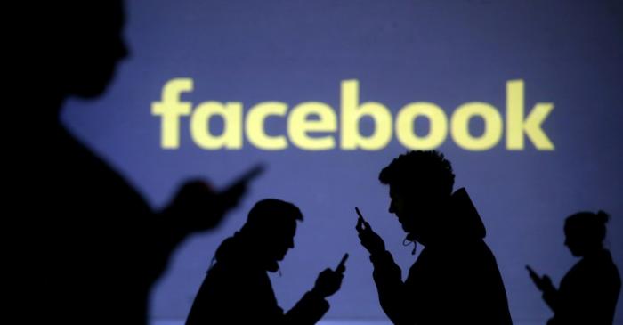 Silhouettes of mobile users are seen next to a screen projection of the Facebook logo in this