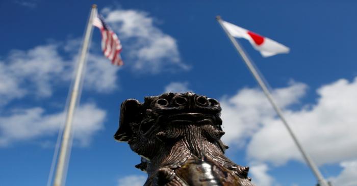 The U.S. and Japanese national flags are hoisted next to a traditional Okinawan Shisa statue at