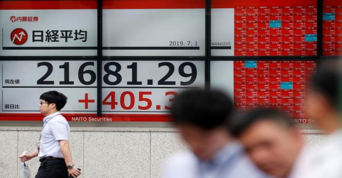 Passerbys walk past an electric screen showing Japan's Nikkei share average outside a brokerage