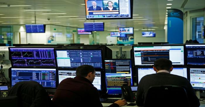 Traders work at their desks whilst screens show market data at CMC Markets in London