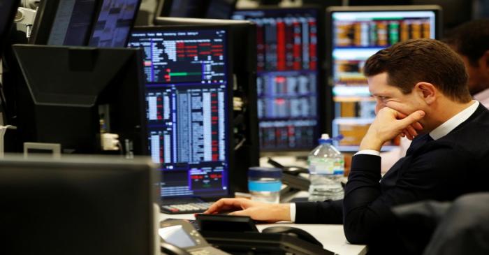 Traders work at their desks whilst screens show market data at CMC Markets in London