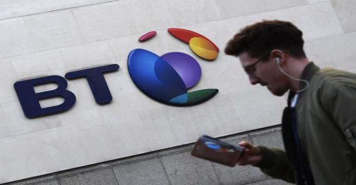 A man walks past a BT logo outside of offices in the City of London