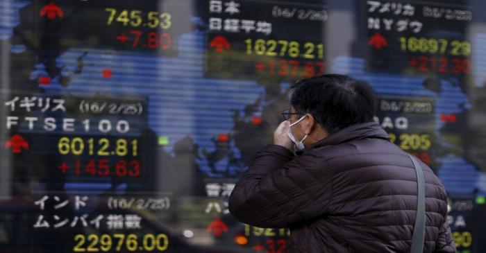 A pedestrian looks at an electronic board showing the stock market indices of various countries