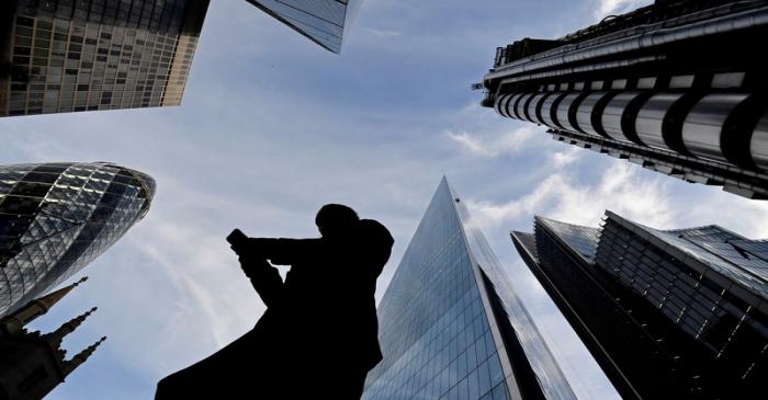 FILE PHOTO: A worker looks at their phone as they walk past The Gherkin, Lloyds, and other