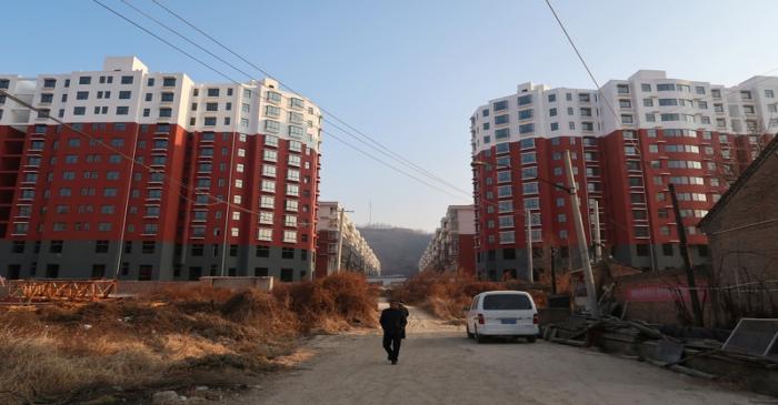 Man walks near a shantytown to be redeveloped, in front of apartment buildings, in Fu county in