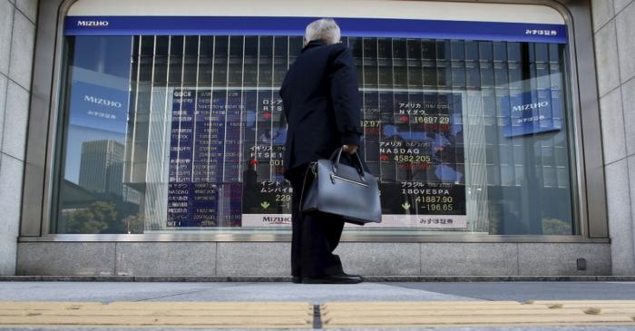 A pedestrian stands to look at an electronic board showing the stock market indices of various