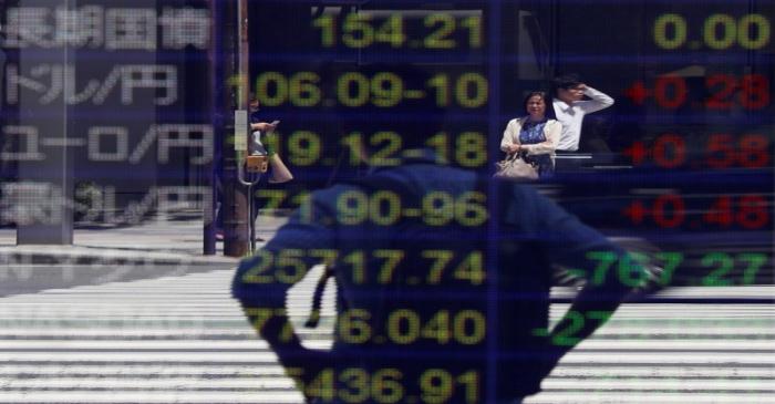 Passersby are reflected on an electronic board showing the exchange rates between the Japanese