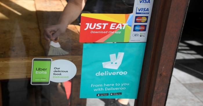 Signage for Just Eat is seen next to Uber Eats and Deliveroo advertisements on the window of a