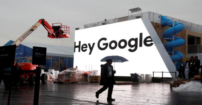 A man walks through light rain in front of the Hey Google booth under construction at the Las