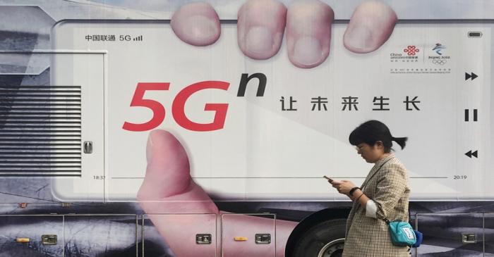 Woman using her mobile phone walks past a vehicle covered in a China Unicom 5G advertisement in