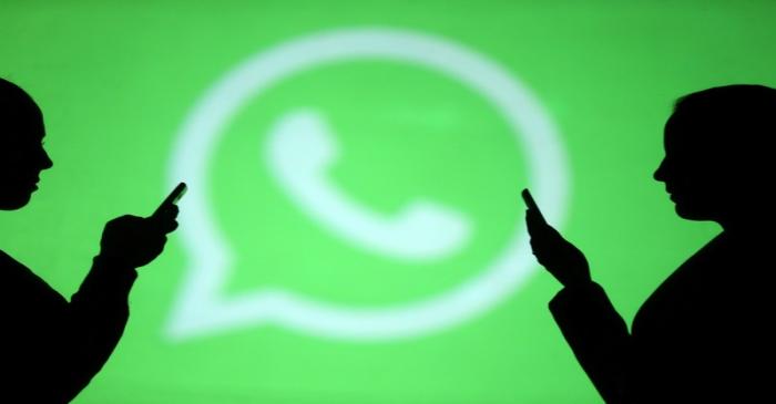 Silhouettes of mobile users are seen next to a screen projection of Whatsapp logo in this
