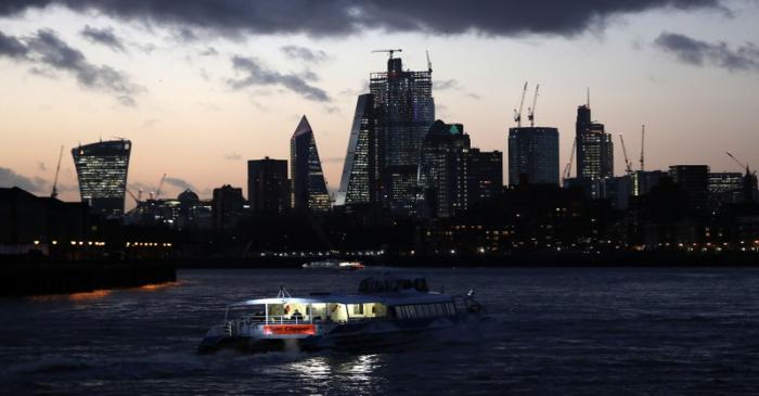 A river boat cruises down the River Thames as the sun sets behind the Canary Wharf financial